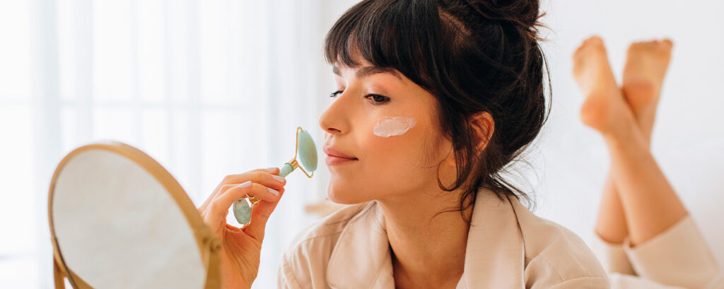 Mujer aplicando crema facial con rodillo de jade después de usar hielo en la cara para mejorar la circulación