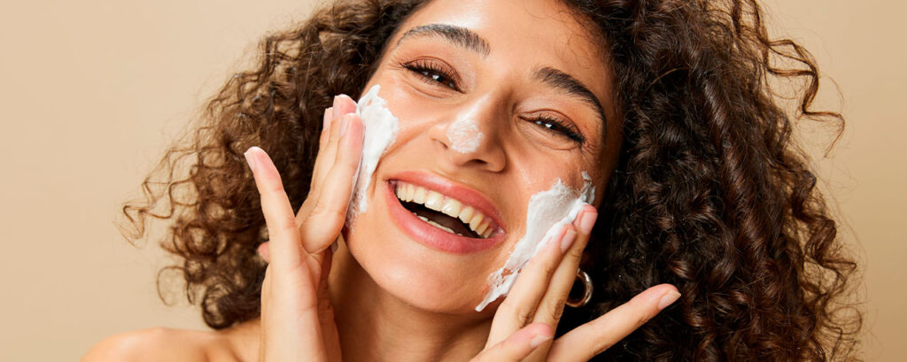 Mujer con piel rizada aplicando crema hidratante en su rostro