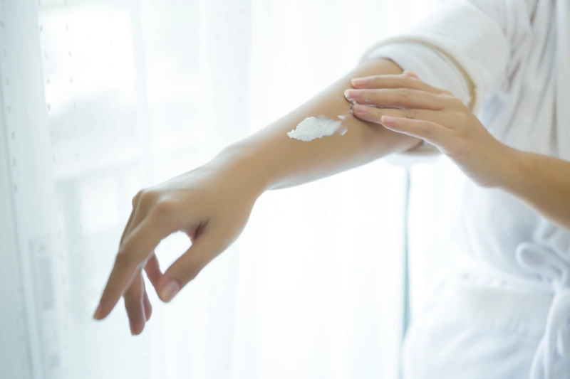 Mujer realizando su rutina de cuidado del cuerpo al aplicar crema en sus brazos con movimientos suaves