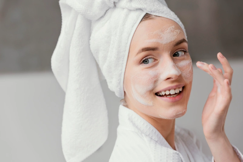 Mujer joven lleva bata de baño y realiza su limpieza facial que cubre todo su rostro