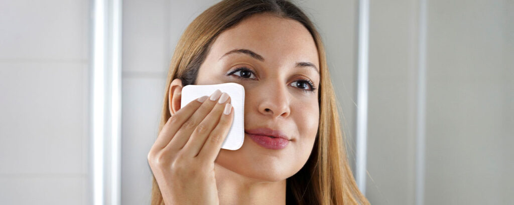 Mujer joven usando un pad facial para limpiar su piel en su rutina diaria de cuidado facial