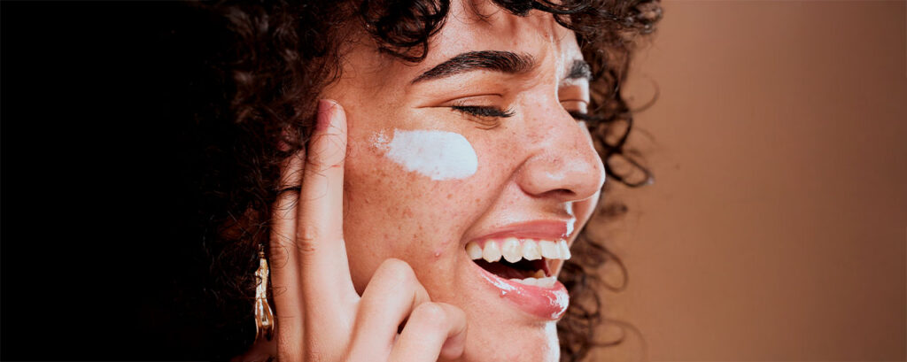 Mujer con piel radiante aplicando crema hidratante como parte de su rutina de cuidado de la piel. 