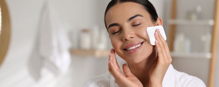 Mujer con bata blanca aplicando su rutina de cuidado de la piel con un pad facial en un ambiente relajante