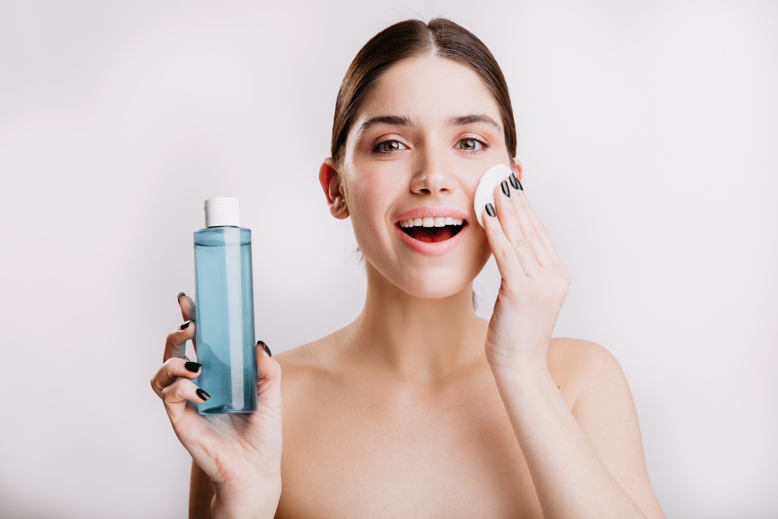 Mujer aplicando agua micelar con un pad facial de algodón para desmaquillar su rostro.