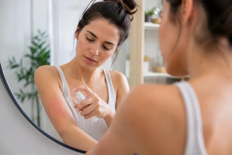 Mujer aplicando spray sobre el brazo para calmar una alergia en la piel.